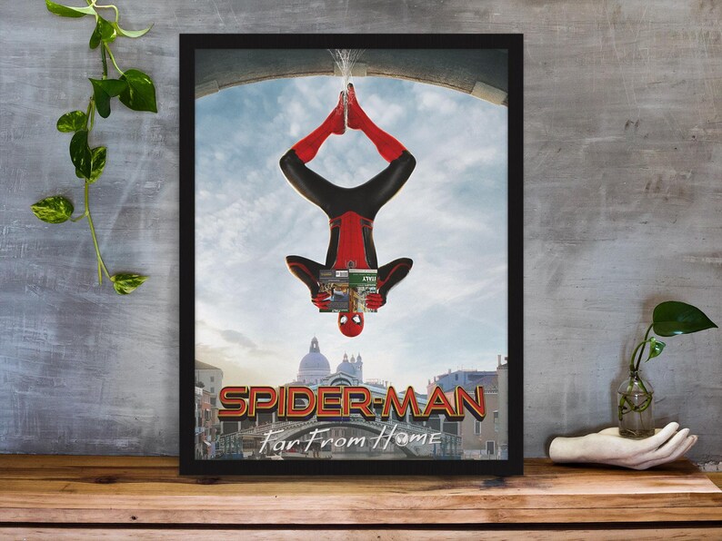 May include: Framed poster featuring Spider-Man in a red and black suit, hanging upside down. The poster has the title "Spider-Man: Far From Home" with a cityscape background and a blue sky. The poster is in a black frame.
