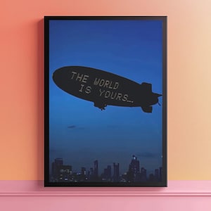 Puede incluir: Impresión artística enmarcada que muestra un dirigible silueteado contra un cielo azul oscuro. El dirigible tiene el texto "THE WORLD IS YOURS..." en blanco. Debajo del dirigible se ve una silueta de la ciudad.