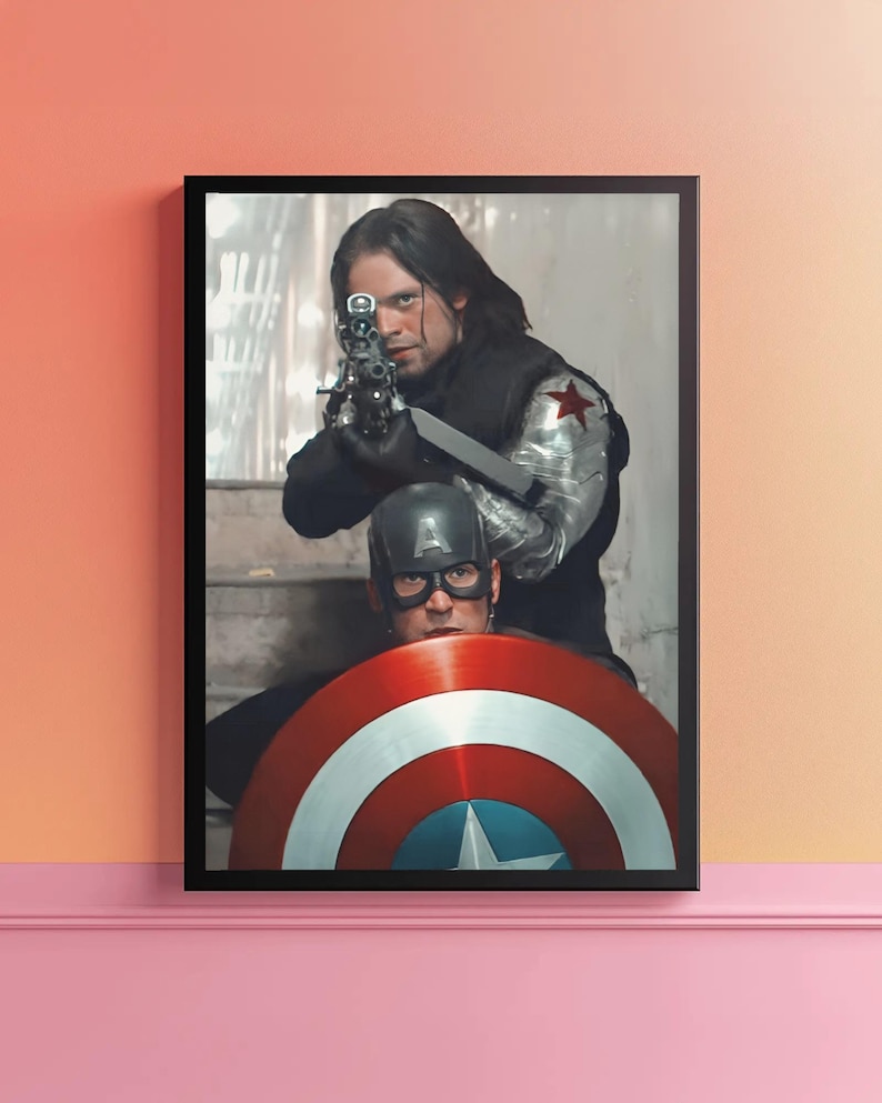 May include: Framed print featuring two characters from a superhero movie. One character aims a gun, while the other holds a shield with red, white, and blue stripes and a central star. The print is in a black frame.