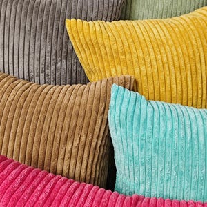 May include: Close-up of a collection of corduroy pillows in various colors. The pillows are in shades of gray, yellow, brown, teal, green, and pink. The corduroy fabric has a ribbed texture.