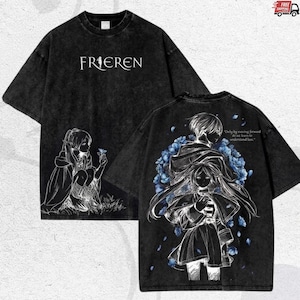 Puede incluir: Camiseta gr&aacute;fica negra con la palabra "FRIEREN" en blanco. La parte delantera muestra una ilustraci&oacute;n blanca de un personaje con una flor. La parte trasera tiene una ilustraci&oacute;n detallada con detalles florales azules y la cita, "Only by moving forward do we learn to understand loss."
