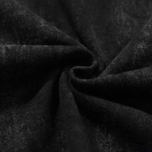 Puede incluir: Primer plano de tela negra con un aspecto texturizado y ligeramente descolorido. El material est&aacute; doblado y drapeado, creando sombras y resaltando la textura de la tela. El efecto general sugiere una prenda o textil.