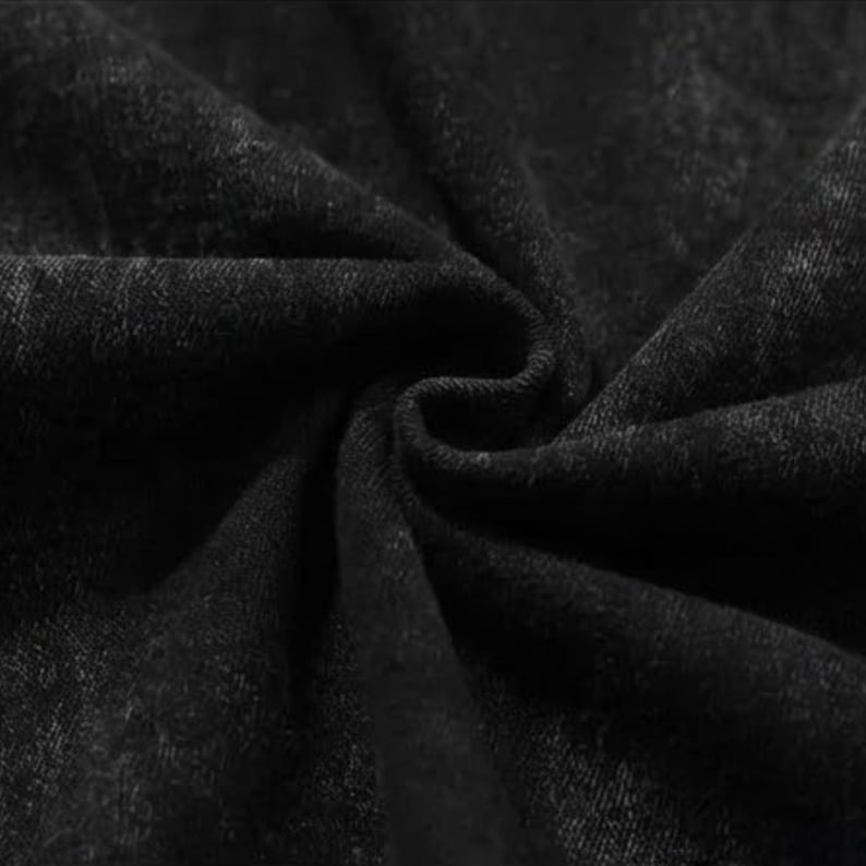 Puede incluir: Primer plano de tela negra con un aspecto texturizado y ligeramente descolorido. El material est&aacute; doblado y drapeado, creando sombras y resaltando la textura de la tela. El efecto general sugiere una prenda o textil.