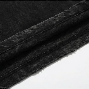Puede incluir: Primer plano de tela vaquera negra, que muestra la textura y los detalles de las costuras. El denim tiene un aspecto descolorido, con costuras visibles y un borde sin rematar. La tela est&aacute; ligeramente arrugada, lo que sugiere que es parte de una prenda.