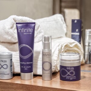May include: A collection of skincare products, including a cleanser, serum, and cream, arranged on a wooden surface. The products are in purple and silver packaging, with the brand name "infinite" and a stylized infinity symbol. White towels are in the background.
