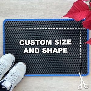 May include: A rectangular black mat with a blue border, featuring a diamond pattern. The text "CUSTOM SIZE AND SHAPE" is displayed in white. White sneakers are placed on the left side. Scissors are on the right side, suggesting customization.