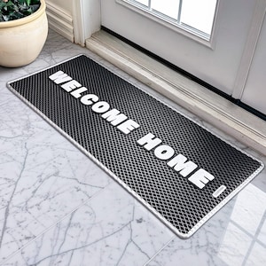 May include: A rectangular black doormat with a diamond pattern and a white border. The words "WELCOME HOME" are printed in bold white letters across the mat. The mat is placed in front of a white door.