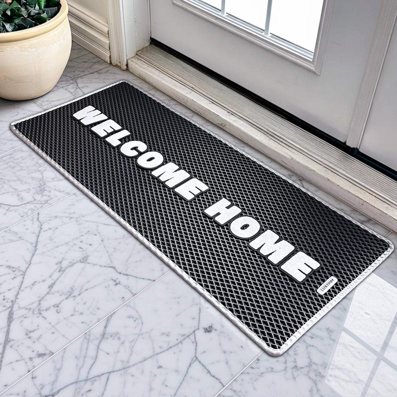 May include: A rectangular black doormat with a diamond pattern and a white border. The words "WELCOME HOME" are printed in bold white letters across the mat. The mat is placed in front of a white door.