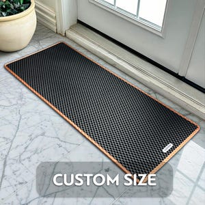 May include: A rectangular black doormat with a diamond pattern and a copper-coloured border. The mat is placed in front of a white door on a marble tile floor. The text "CUSTOM SIZE" is displayed on the mat.