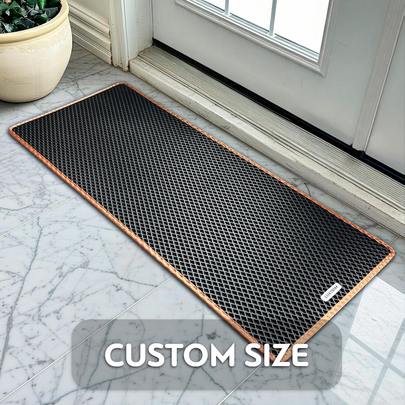 May include: A rectangular black doormat with a diamond pattern and a copper-coloured border. The mat is placed in front of a white door on a marble tile floor. The text "CUSTOM SIZE" is displayed on the mat.