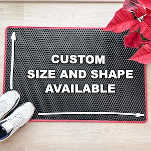 May include: A black rectangular doormat with a diamond pattern and a red border. The text "CUSTOM SIZE AND SHAPE AVAILABLE" is displayed in white. White arrows and lines indicate the custom sizing. White trainers are visible in the lower left corner.