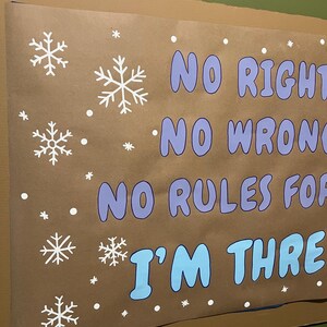 May include: A brown poster with white snowflakes and the text "NO RIGHT, NO WRONG, NO RULES FOR, I'M THREE" in blue and purple. The poster is mounted on a green wall.