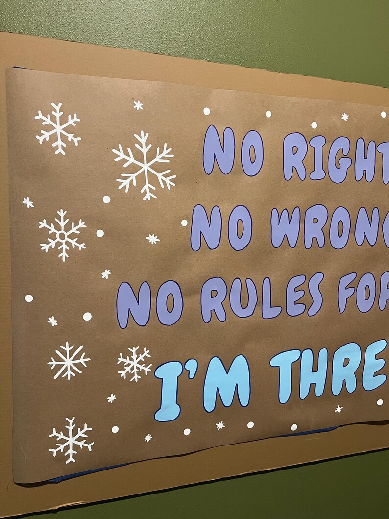 May include: A brown poster with white snowflakes and the text "NO RIGHT, NO WRONG, NO RULES FOR, I'M THREE" in blue and purple. The poster is mounted on a green wall.