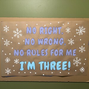 May include: A brown paper sign with the text "NO RIGHT, NO WRONG, NO RULES FOR ME I'M THREE!" in blue and white. White snowflakes and dots are scattered across the sign.