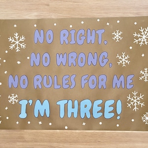 Puede incluir: Un letrero rectangular marr&oacute;n con el texto "NO RIGHT, NO WRONG, NO RULES FOR ME I'M THREE!" en azul y morado. Copos de nieve y puntos blancos decoran el letrero.
