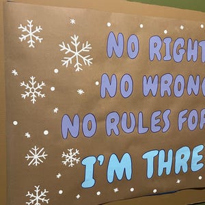 Puede incluir: Un cartel marr&oacute;n con copos de nieve blancos y el texto "NO RIGHT, NO WRONG, NO RULES FOR, I'M THREE" en azul y morado. El cartel est&aacute; montado en una pared verde.