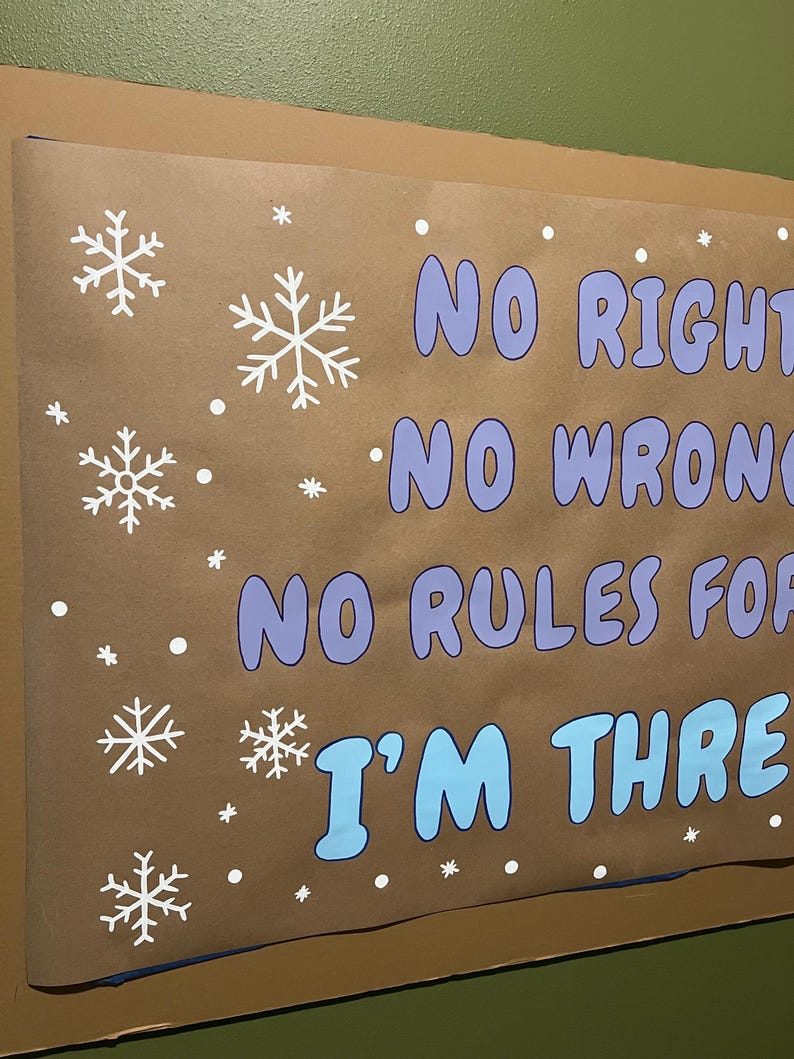 Puede incluir: Un cartel marr&oacute;n con copos de nieve blancos y el texto "NO RIGHT, NO WRONG, NO RULES FOR, I'M THREE" en azul y morado. El cartel est&aacute; montado en una pared verde.