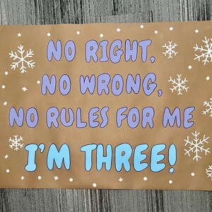May include: A brown paper sign with the text "NO RIGHT, NO WRONG, NO RULES FOR ME I'M THREE!" in blue and purple lettering. White snowflakes and dots surround the text.