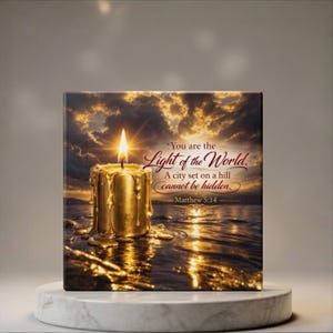 Puede incluir: Impresión en lienzo cuadrada que presenta una vela dorada encendida con cera goteando, sobre un fondo de puesta de sol sobre el agua. El texto "You are the Light of the World" y Mateo 5:14 son visibles.