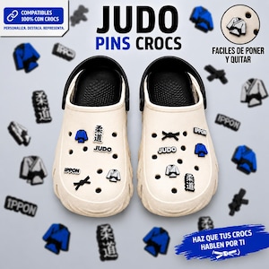 Könnte beinhalten: Beige Crocs mit schwarzen Akzenten, verziert mit Judo-Pins. Die Pins zeigen einen blauen Gi, einen schwarzen Gürtel und das Wort "JUDO". Zusätzliche Pins zeigen das Wort "IPPON" und japanische Schriftzeichen.