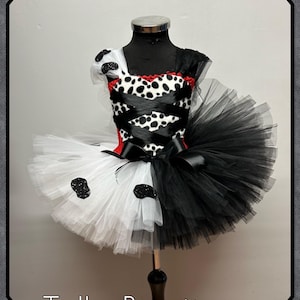 Puede incluir: Vestido tutú blanco y negro con corpiño con estampado de dálmata y falda de tul en capas. El vestido tiene un ribete rojo y detalles de lazo negro. El texto "Tulle Boutique" está en la parte inferior.
