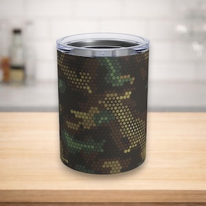 May include: A cylindrical travel tumbler with a camouflage pattern in shades of brown, green, and yellow. The tumbler has a silver rim and a clear lid. The design is made up of small, hexagonal shapes.