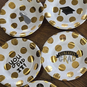 May include: Set of ten white paper plates with gold polka dots and graduation-themed text. The plates feature phrases like "Congrats Grad", "You Did It!" and "Good Luck in Your Next Adventure".