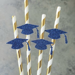 May include: A collection of gold and white striped paper straws, each adorned with a blue glitter graduation cap. The caps have a tassel and are a vibrant blue color. The straws are arranged in a close-up shot, perfect for a graduation party.