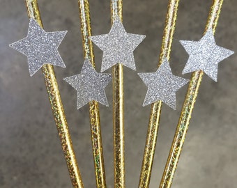 May include: Six gold straws with silver glitter stars at the top. The straws are iridescent and have a shiny finish.