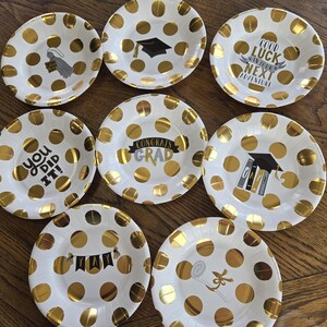 May include: Set of 8 white paper plates with gold polka dots and graduation-themed text. The plates feature phrases like "Congrats Grad", "You Did It!" and "Good Luck in Your Next Adventure".