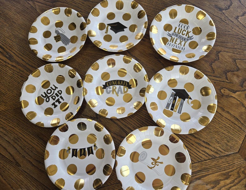 May include: Set of 8 white paper plates with gold polka dots and graduation-themed text. The plates feature phrases like "Congrats Grad", "You Did It!" and "Good Luck in Your Next Adventure".