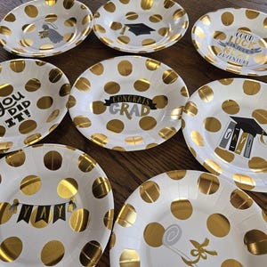 May include: Ten white paper plates with gold polka dots and graduation-themed text. The text on the plates includes "You Did It!", "Congrats Grad", "Good Luck in Your Next Adventure", and "Yay".
