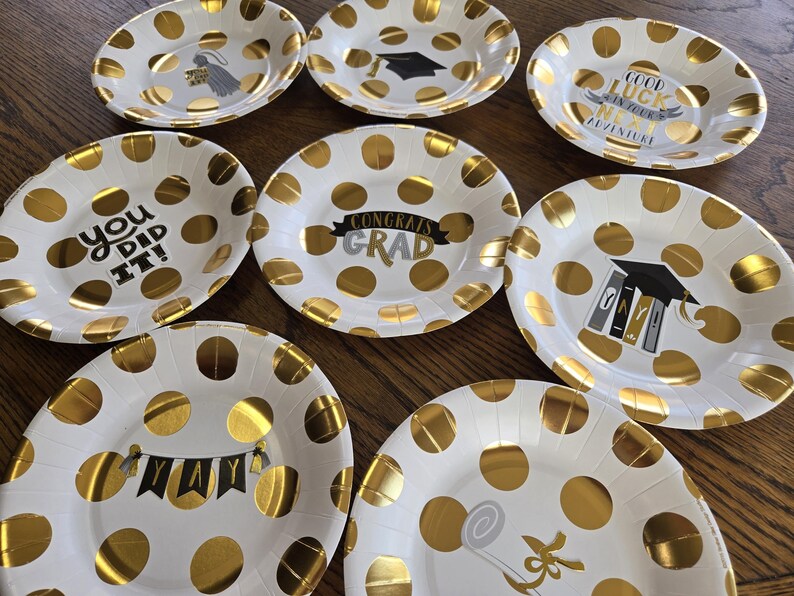 May include: Ten white paper plates with gold polka dots and graduation-themed text. The text on the plates includes "You Did It!", "Congrats Grad", "Good Luck in Your Next Adventure", and "Yay".