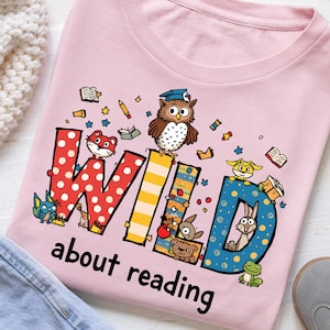 May include: A light pink t-shirt featuring a graphic print with the text "WILD about reading". The word "WILD" is composed of large, colourful, patterned letters decorated with cartoon animals, including an owl wearing a graduation cap.