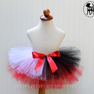 May include: A red, white, and black tulle tutu with a red satin bow. The tutu is on a white mannequin.