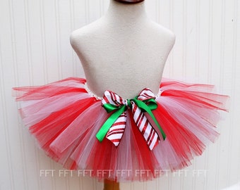 May include: Red and white tulle tutu with a green and red candy cane bow. The tutu is on a white mannequin.