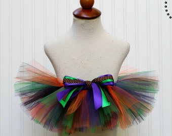 May include: A multi-coloured tulle tutu with a purple, green and brown ribbon bow. The tutu is on a white mannequin.