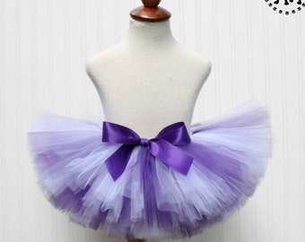 May include: A purple and white tulle tutu with a purple satin bow. The tutu is on a white mannequin.