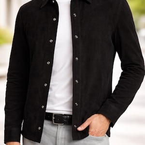 May include: Black suede shirt with silver buttons, worn over a white t-shirt. The outfit includes grey jeans and a black belt. The style is casual and suitable for everyday wear.