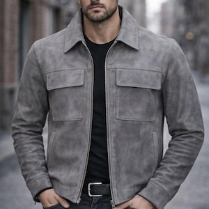 Pu&ograve; includere: Giacca in camoscio grigio con zip, due tasche sul petto e colletto. Indossata sopra una maglietta nera e abbinata a jeans scuri e una cintura nera.