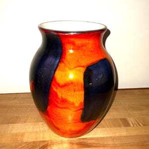 May include: A ceramic vase with a glossy finish. The vase features a vibrant color palette of orange, red, and navy blue. The interior is white. The vase is a decorative item, suitable for displaying flowers or as a standalone art piece.