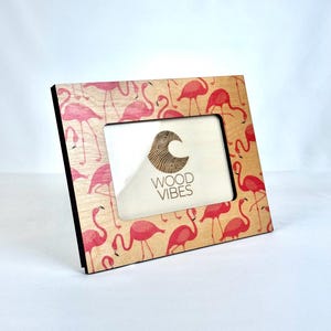 May include: Square wooden picture frame with a flamingo pattern in pink and red on a light brown background. The frame has a black edge and the text "WOOD VIBES" is visible.