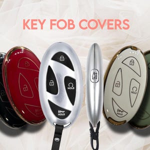 May include: A collection of key fob covers in various colors, including black, red, and silver. The covers feature button designs for lock, unlock, and hold functions. The text "KEY FOB COVERS" is displayed in pink.