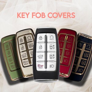 May include: A collection of key fob covers in various colors, including green, cream, red, and navy blue. Each cover has a metallic gold trim. The image also displays the text "KEY FOB COVERS".