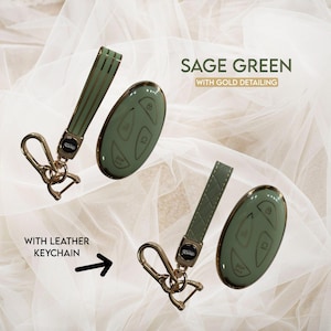 May include: Sage green car key fob with gold detailing and a matching leather keychain. The key fob has gold accents and a smooth finish. The keychain has a gold clasp.