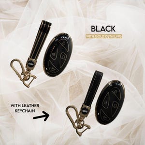 May include: Black car key fobs with gold detailing and leather keychains. The key fobs are oval-shaped with buttons for locking, unlocking, and other functions. The keychains are black with gold accents and a metal clasp.