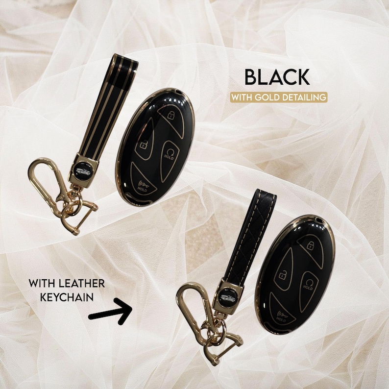 May include: Black car key fobs with gold detailing and leather keychains. The key fobs are oval-shaped with buttons for locking, unlocking, and other functions. The keychains are black with gold accents and a metal clasp.