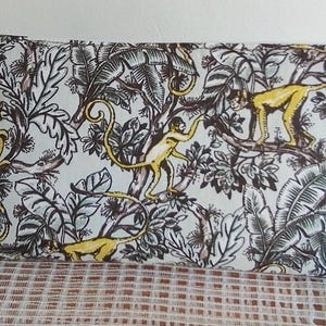 Può includere: Una pochette rettangolare con cerniera con un motivo giungla. Presenta scimmie gialle, rami marroni e foglie verdi e bianche su uno sfondo azzurro.