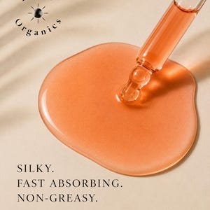 May include: Close-up of a clear glass dropper dispensing a peach-colored liquid onto a light beige surface. The liquid forms a large, glossy puddle. Text reads "Silky. Fast Absorbing. Non-Greasy." and "Lightweight hydration that nourishes and renews."