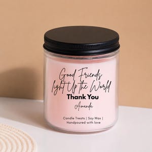 Peut inclure: Une bougie en cire rose clair dans un pot en verre transparent avec un couvercle noir. L'étiquette porte le texte noir suivant : Good Friends light Up the World, Thank You, Amanda, Candle Treats | Soy Wax | Handpoured with love.